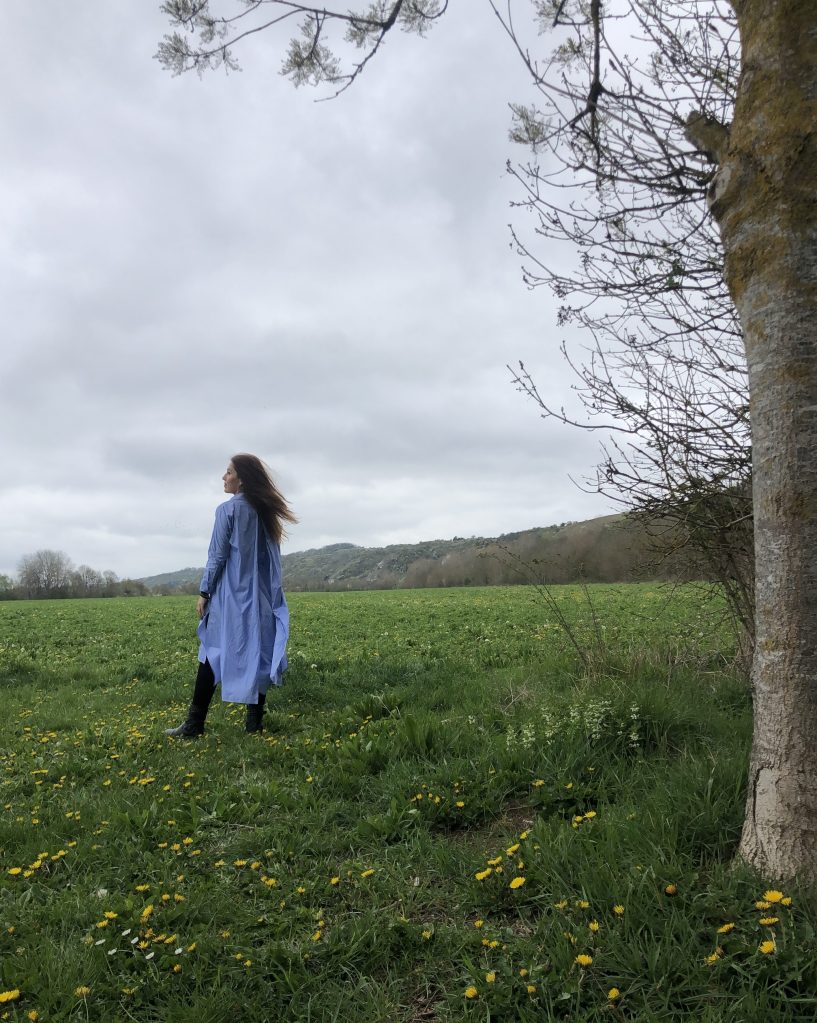 Woman with auburn hair standing in an empty field in France.